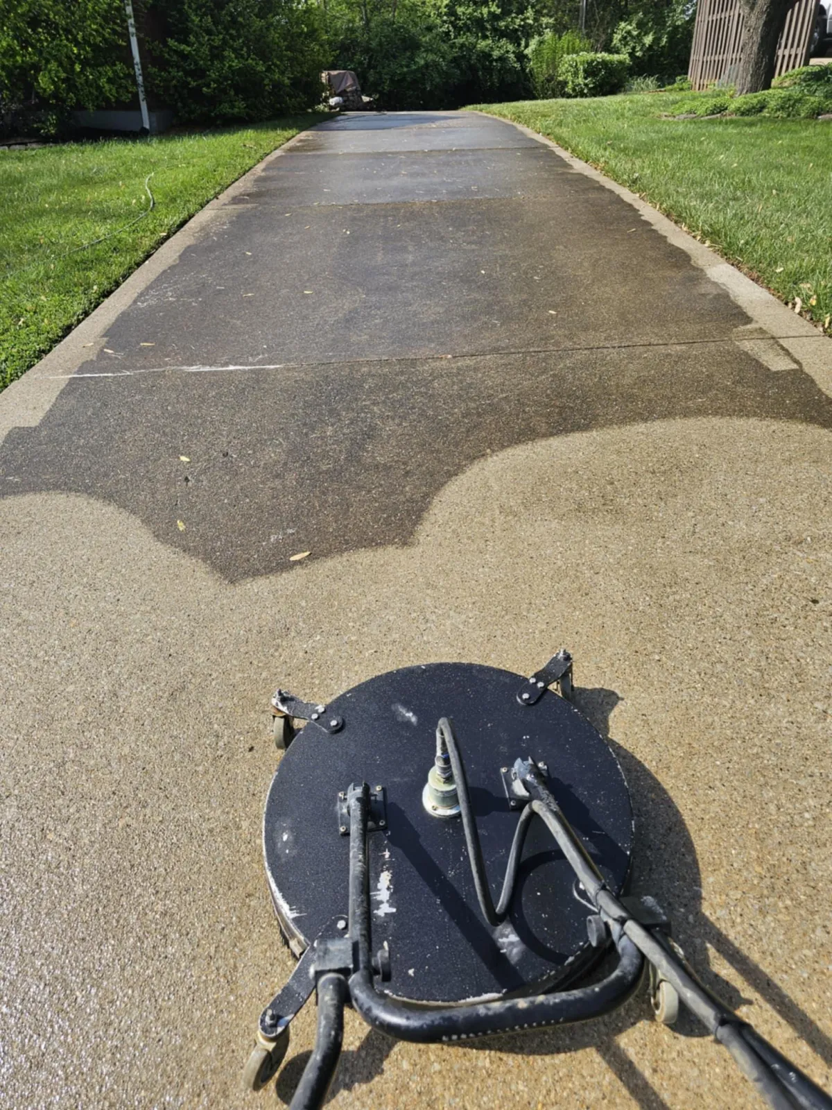 A pressure washer cleans a concrete driveway, showing a clear contrast between cleaned and uncleaned sections.